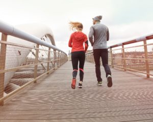 A man in gray an a woman in a red top running together on a bridge