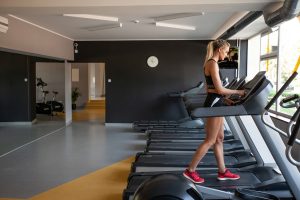 Blond girl running on a treadmill in a room with dark gray walls